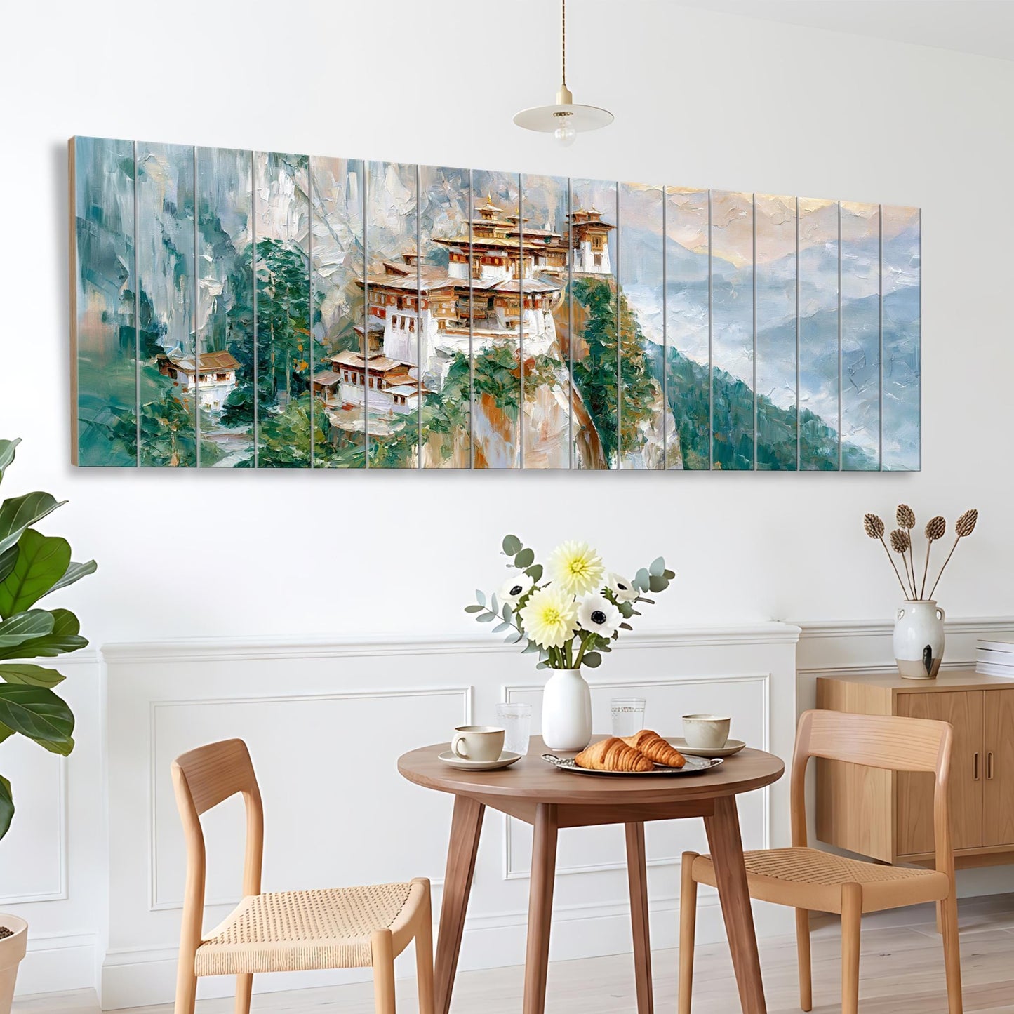 a dining area with a wooden table and chairs, a vase of flowers, and a large painting of a mountain village hanging on the wall above the table.