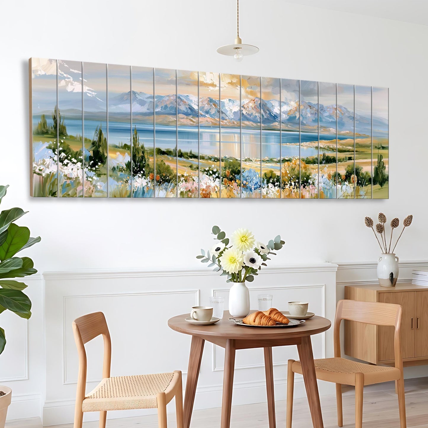 a large, colorful painting of a landscape with mountains, flowers, and a lake, hanging on a wall above a wooden dining table with two chairs.