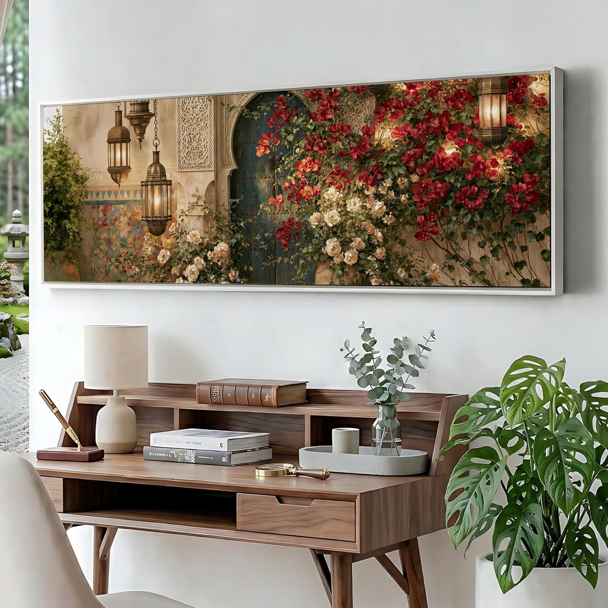 a large, framed painting of a garden scene with red flowers and greenery, hanging on a wall above a wooden desk with a lamp, books, and a vase of flowers.