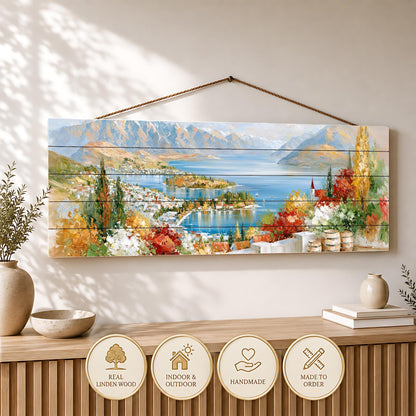 a wooden wall hanging depicting a scenic landscape with mountains, a lake, and a town surrounded by trees.
