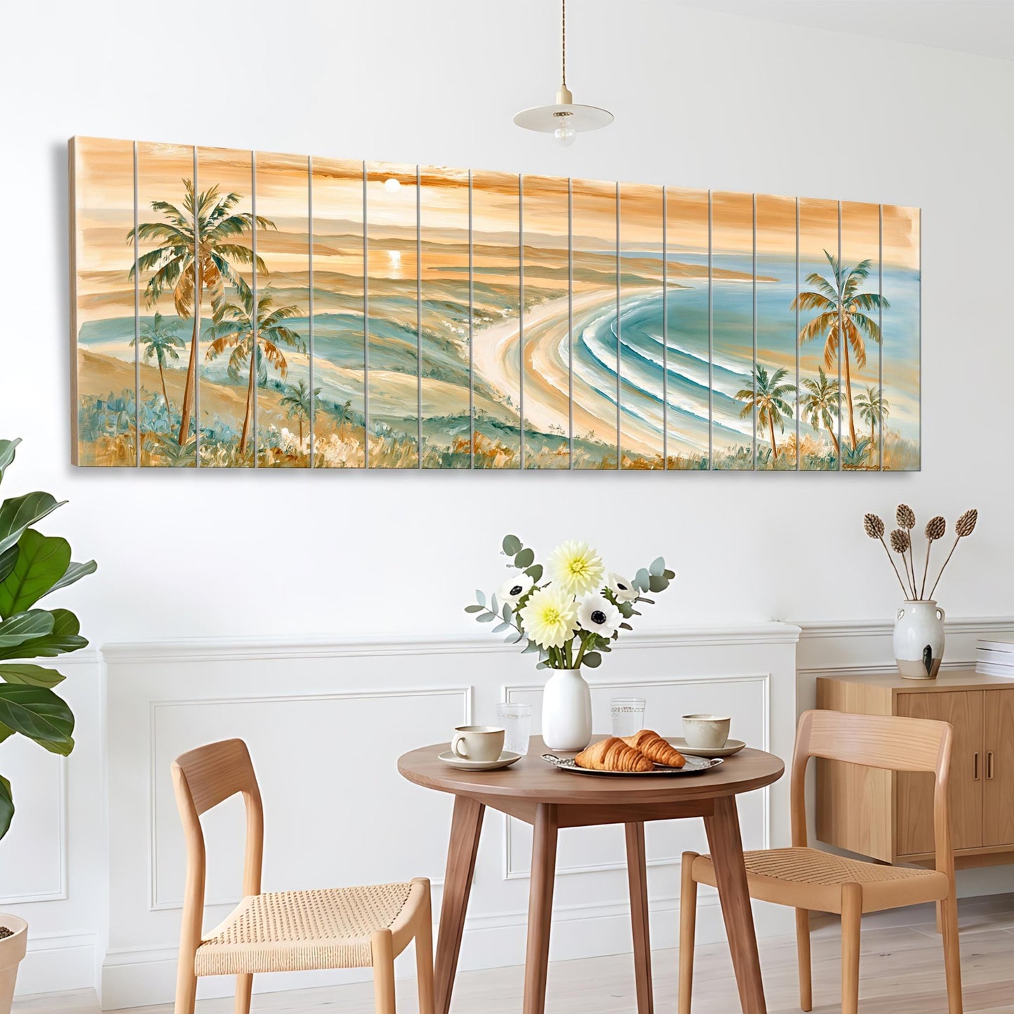 a dining area with a table set for two, featuring a vase of flowers, a plate of pastries, and two chairs. Above the table, there is a large painting depicting a beach scene with palm trees and a sunset.