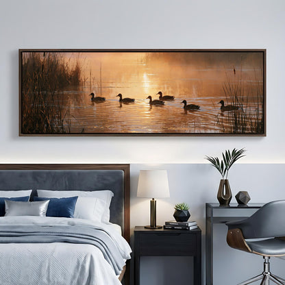 a large painting of ducks swimming in a lake at sunset, hanging on a wall above a bed with a gray headboard.