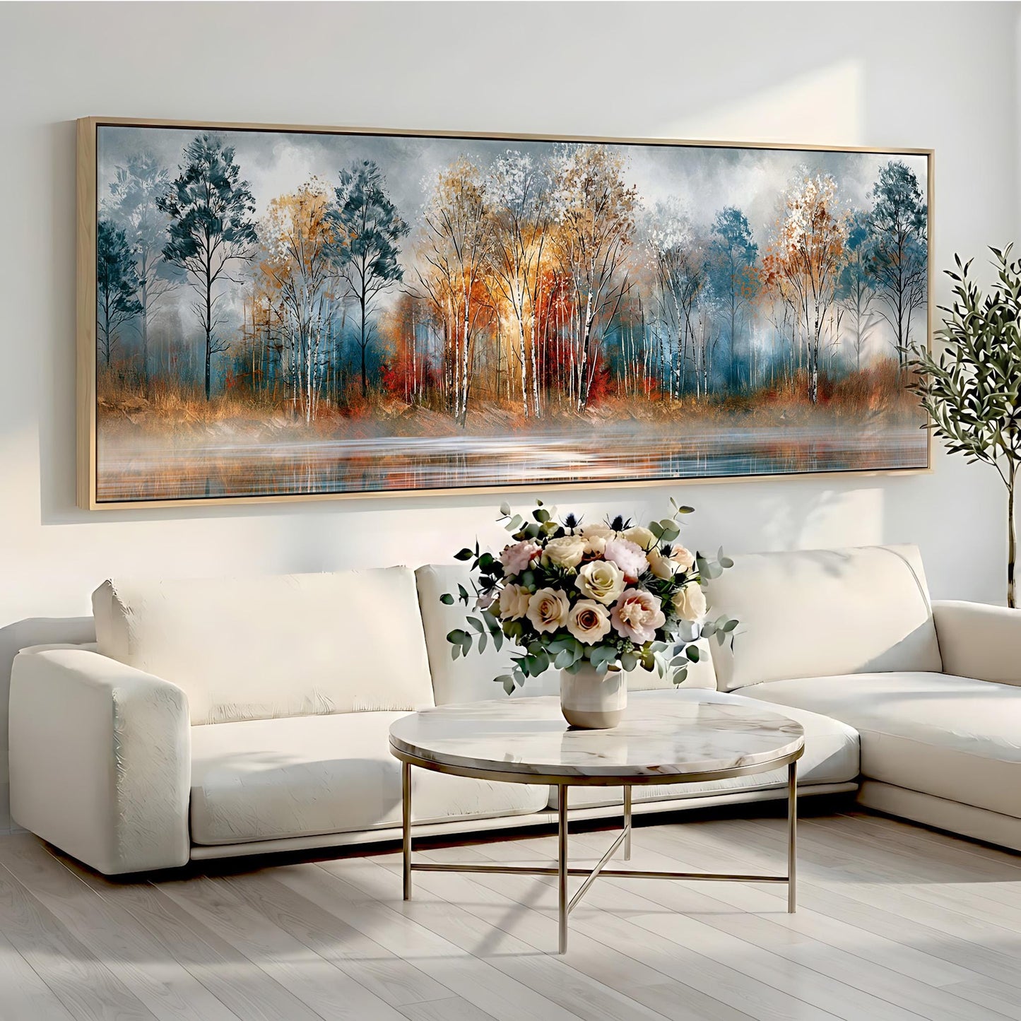 a large painting of a forest scene hanging on a wall above a white sofa and a round coffee table with a vase of flowers.