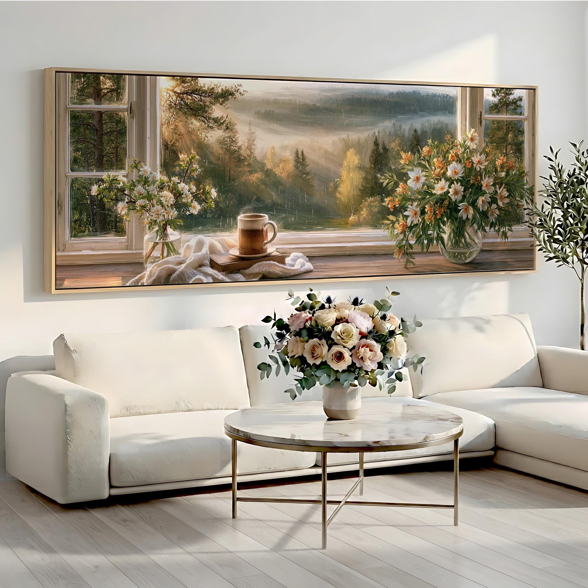 a large painting of a scenic landscape with a coffee cup and flowers on a windowsill, set against a white wall. The painting is framed and hangs above a white sofa and a round coffee table in a cozy living room setting.