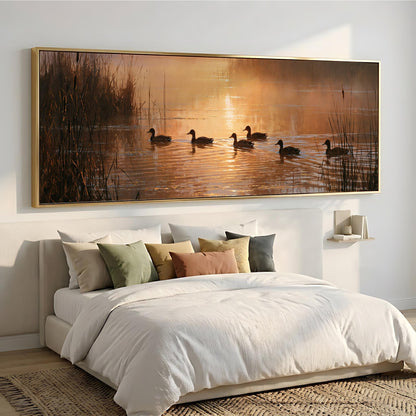 a serene scene of ducks swimming on a lake at sunset, with a large framed painting hanging above a bed with white bedding and pillows.
