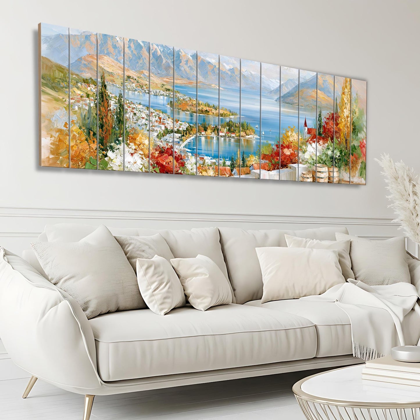 a large, colorful painting of a scenic landscape with mountains, a lake, and a town, hanging on a wall above a white sofa in a living room.