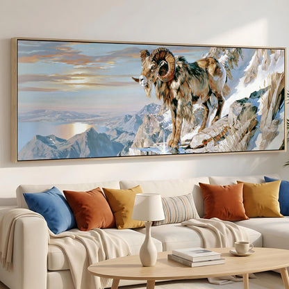 a large painting of a ram standing on a snowy mountain, mounted on a wall above a white couch with colorful throw pillows.