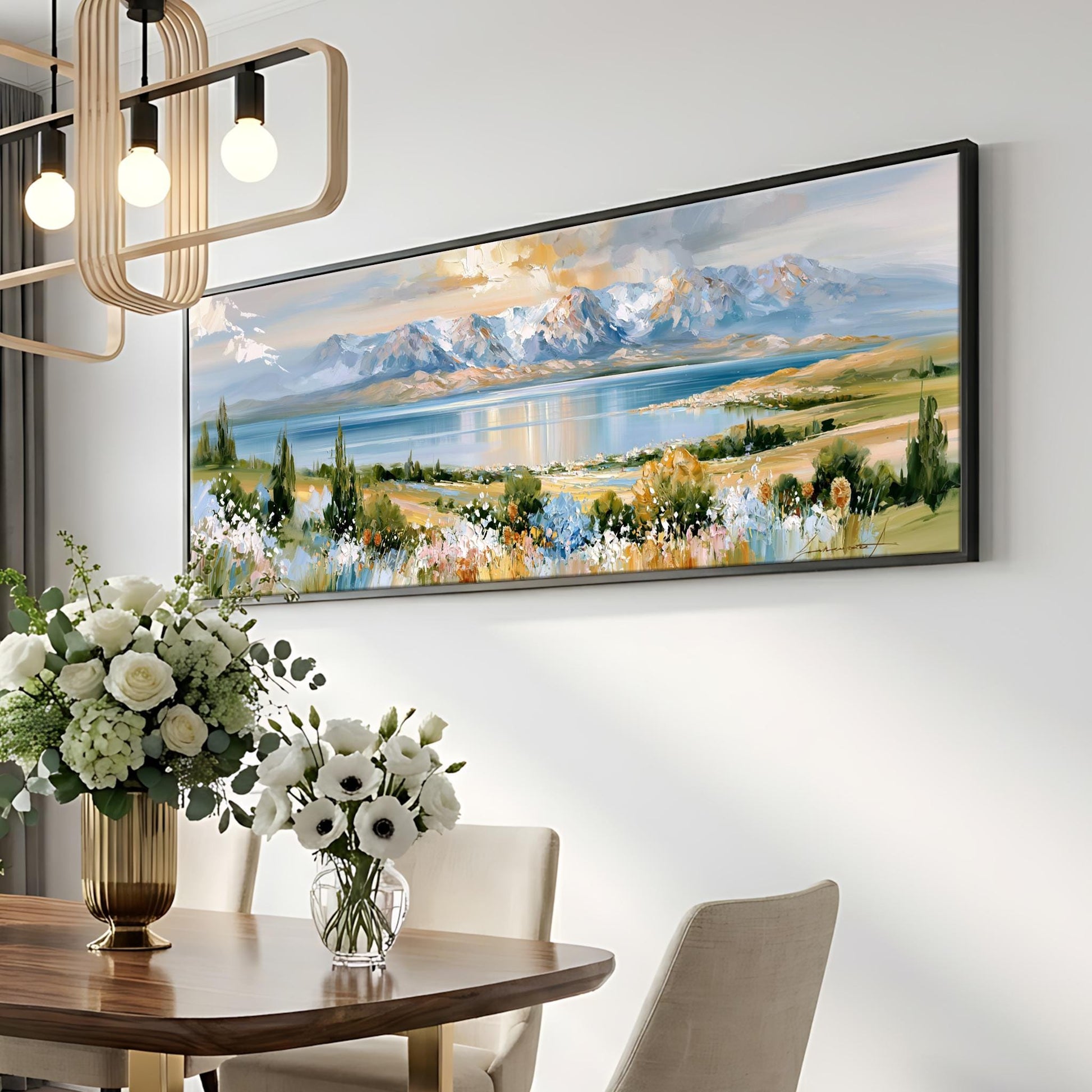 a large landscape painting hanging on a wall above a dining table with a vase of white flowers.