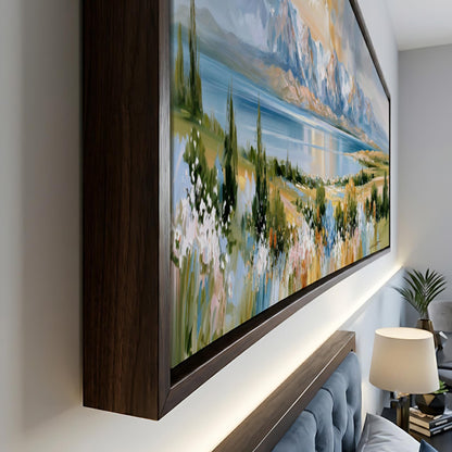 a large, framed painting of a scenic landscape with mountains, trees, and a body of water. The painting is displayed on a wall, and there is a lamp and a couch in the foreground.