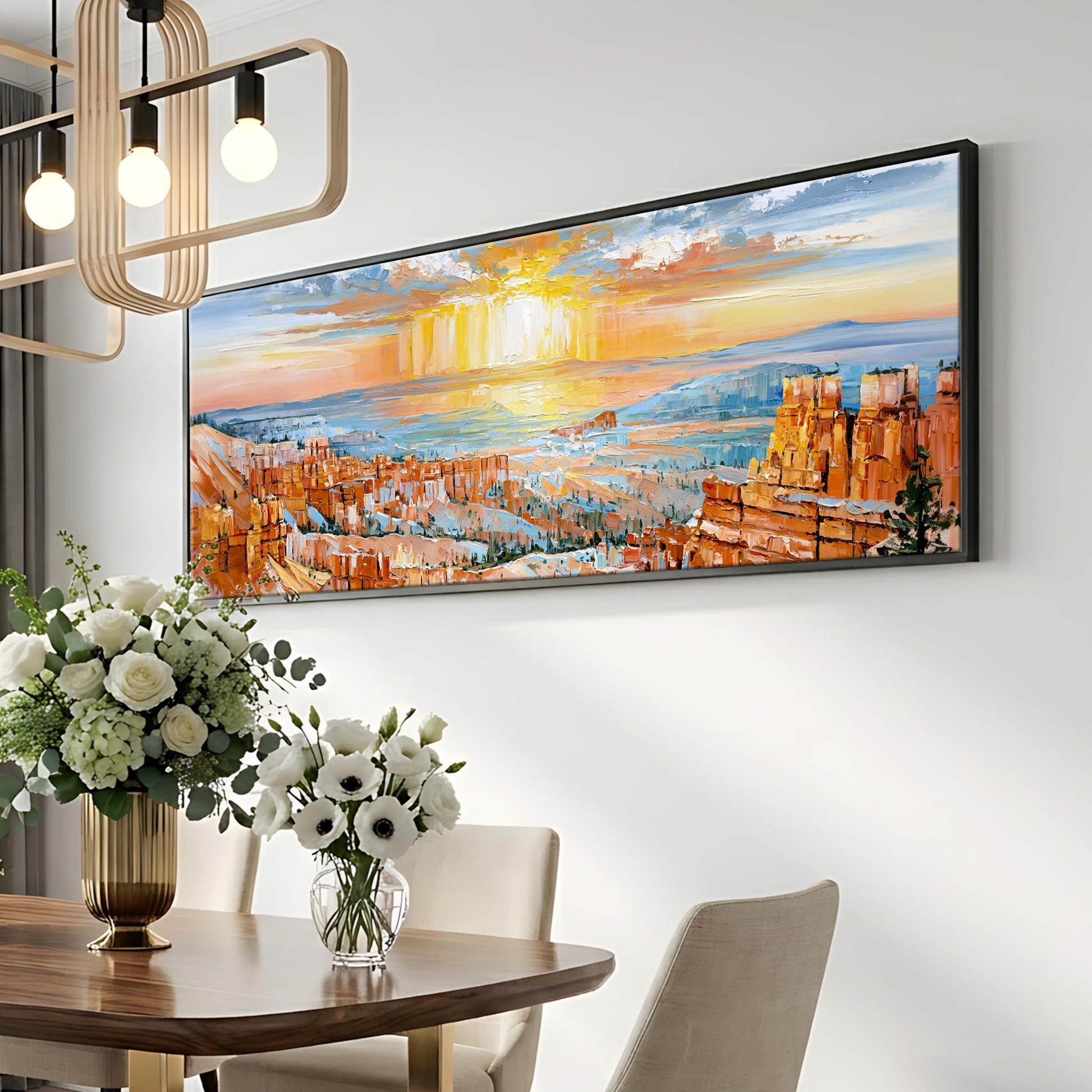 a large, colorful painting of a desert landscape hanging on a wall above a dining table with a vase of white flowers.