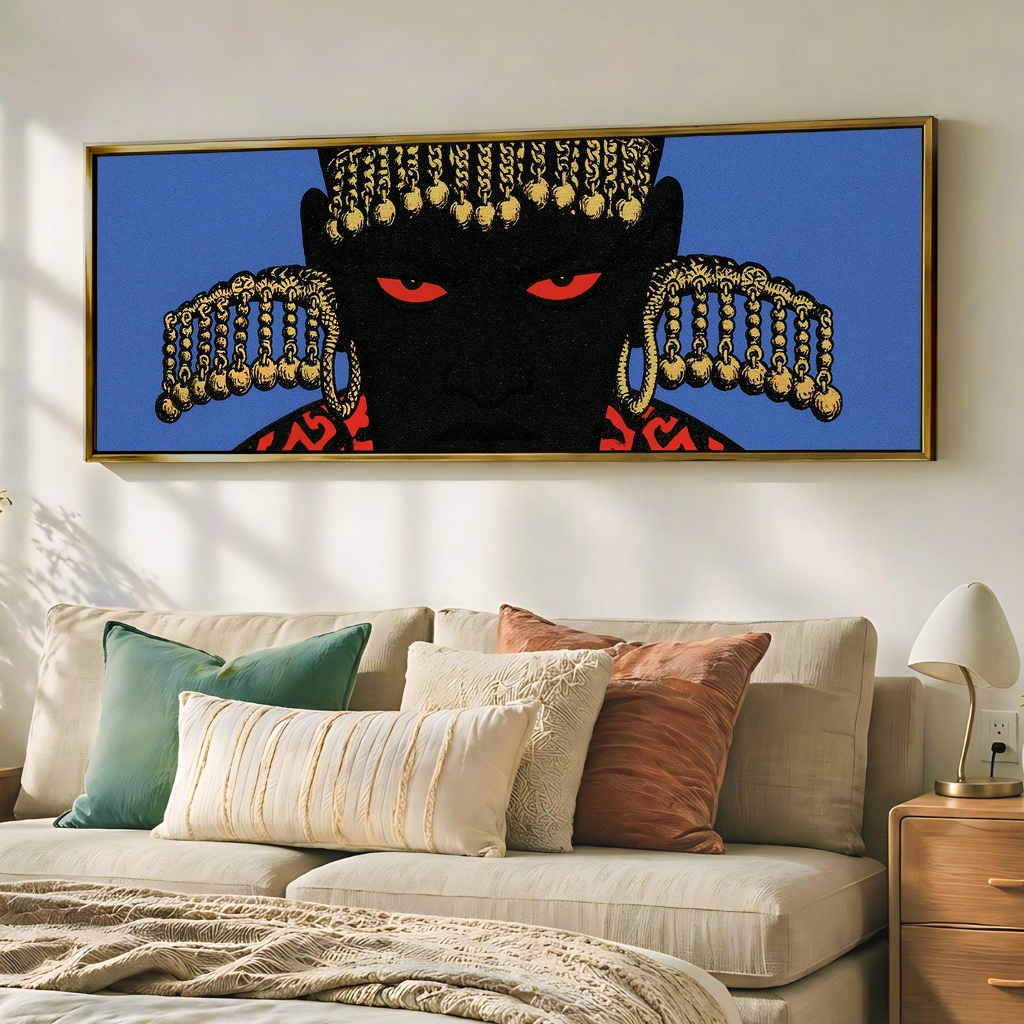 a large framed artwork depicting a black figure with red eyes and gold ornaments, hanging on a wall above a beige couch with various pillows.