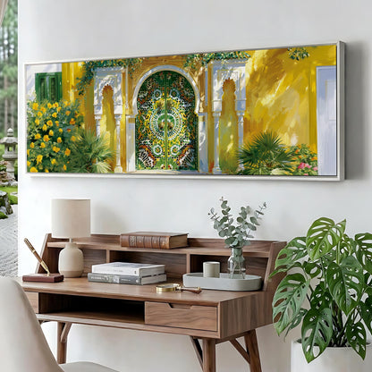 a large, colorful painting of a yellow building with a green archway, hanging on a wall above a wooden desk with a lamp, books, and a vase of greenery.