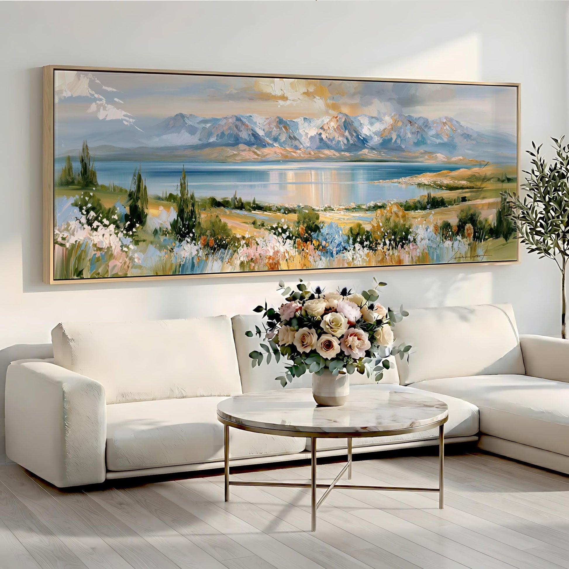 a large landscape painting hanging on a wall above a white sofa and a round coffee table with a vase of flowers.