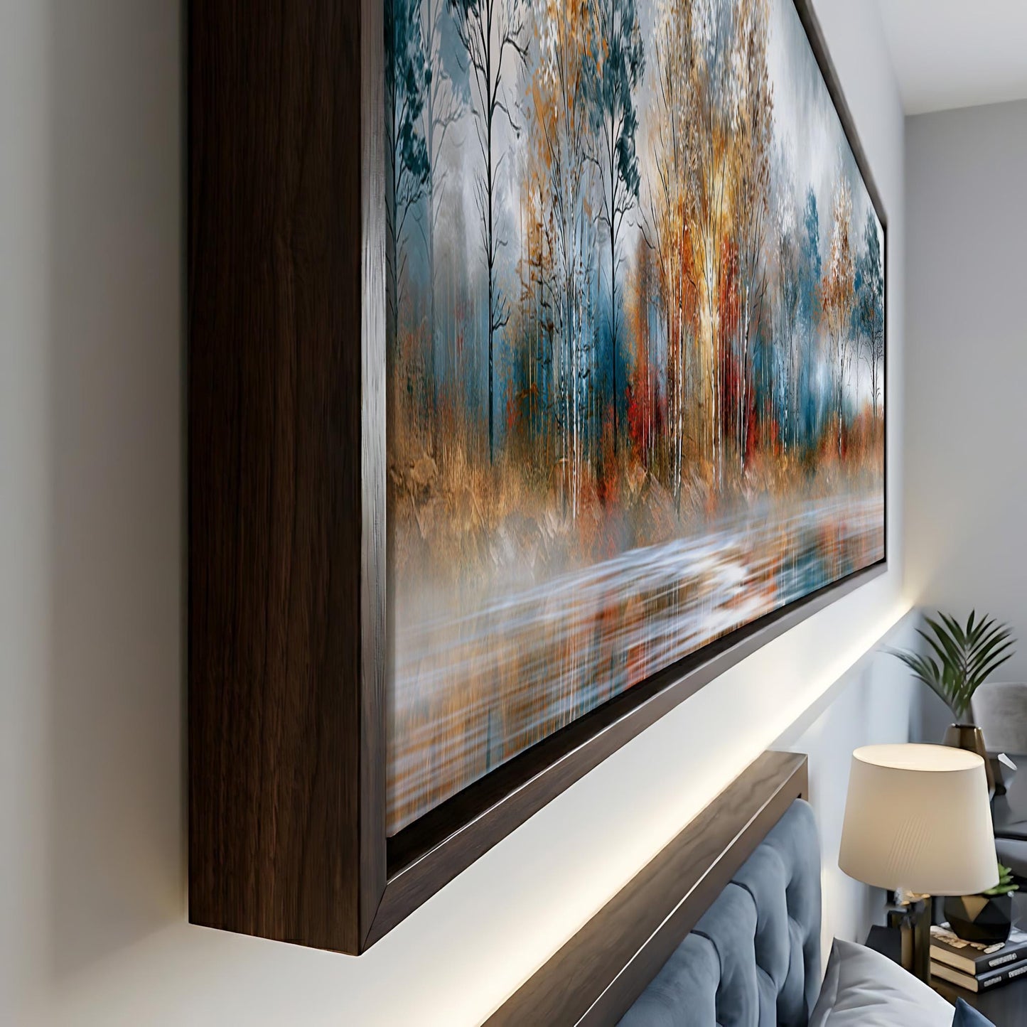 a large, framed painting of a forest scene with a mix of blue, orange, and green colors. The painting is displayed on a wall, and there is a lamp and a plant in the foreground.