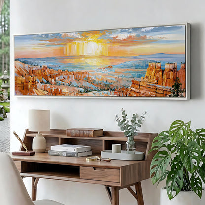 a large painting of a scenic landscape with a sunset over a city, hanging on a wall above a wooden desk with a lamp, books, and a plant.