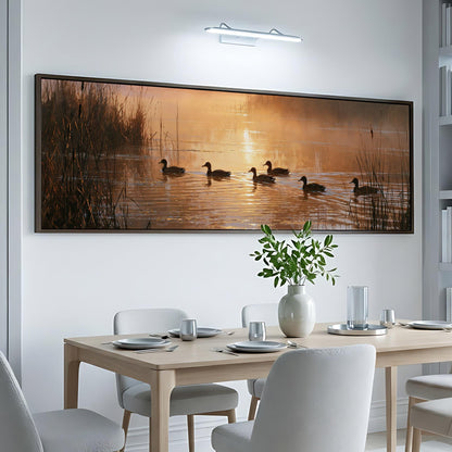 a large, framed painting of ducks swimming on a lake, with a warm sunset in the background. The painting is hung on a white wall above a dining table set with plates, silverware, and a vase of flowers.