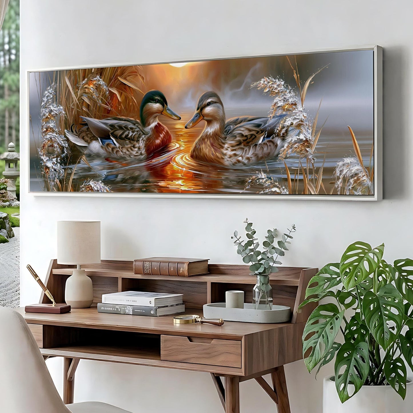 a large painting of ducks swimming in a pond, hanging on a wall above a wooden desk with various items on it.