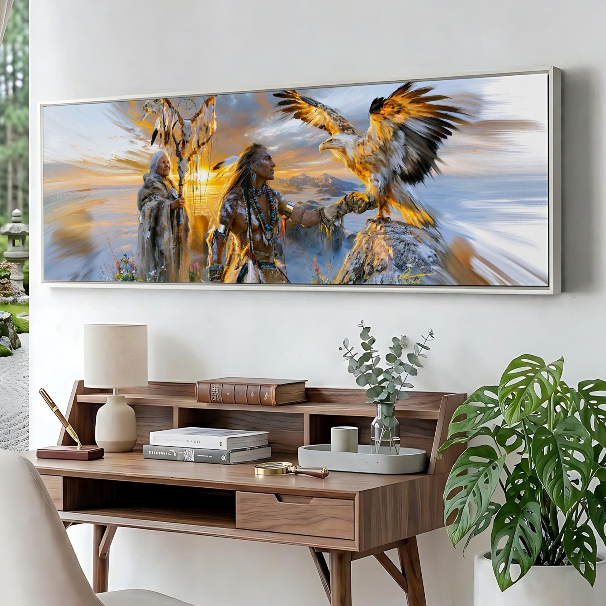 a large framed painting depicting a Native American scene with a bird of prey, a person, and a landscape with a sunset. The painting is displayed on a wall above a wooden desk with various items on it, including a lamp, books, and a vase with greenery.