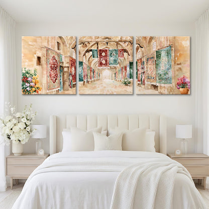 A large, three-panel painting depicting a hallway with arched doorways and colorful tapestries hanging on the walls. The painting is displayed on a white wall above a bed with white bedding and pillows.