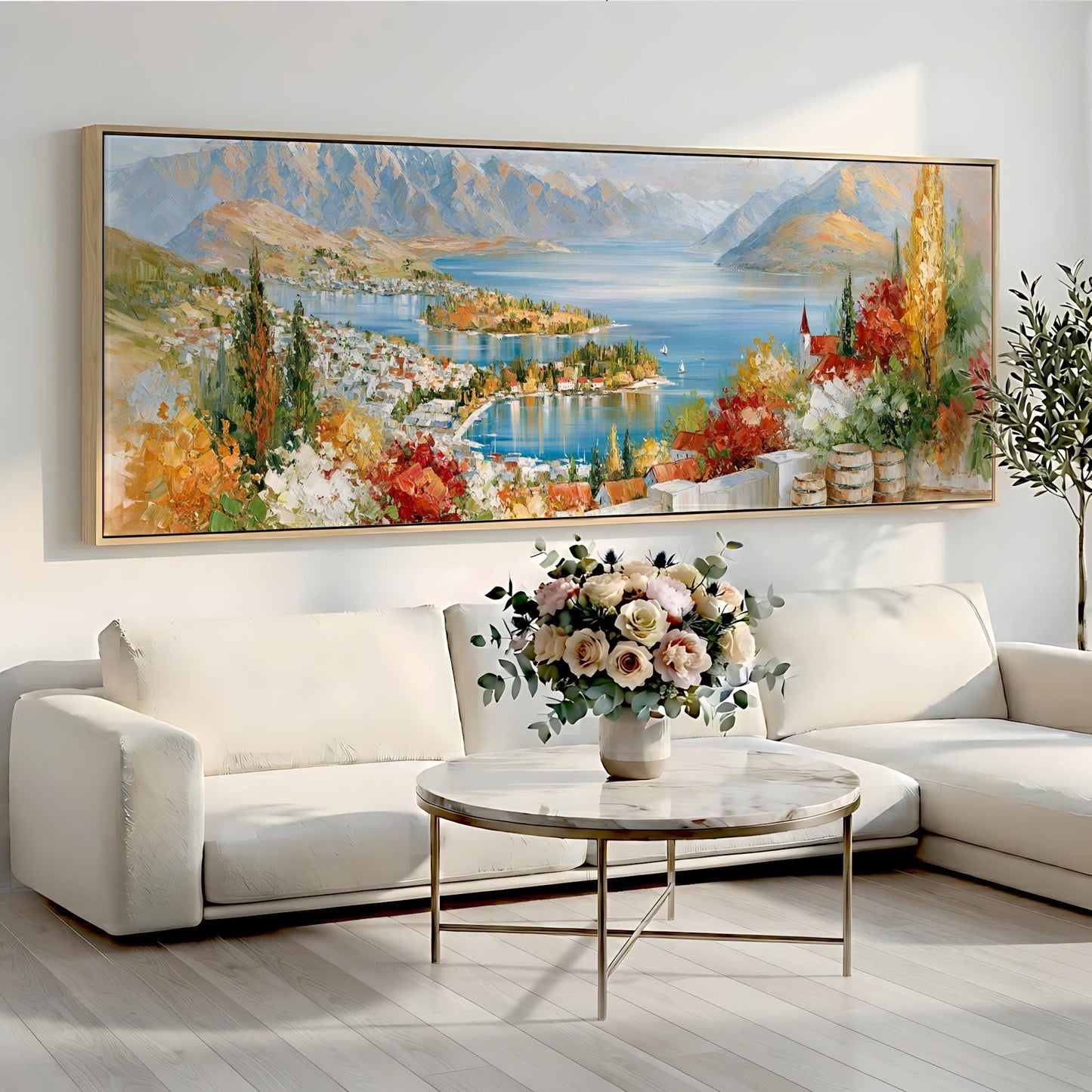 a large, colorful painting of a scenic landscape hanging on a wall above a white sofa and a round coffee table with a vase of flowers.