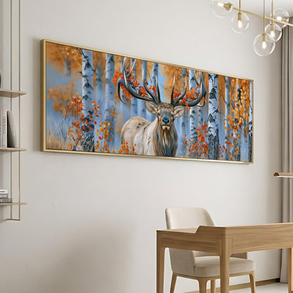 a large framed painting of a deer with antlers, set against a background of trees with orange leaves, hanging on a wall in a room with a wooden desk and chair.
