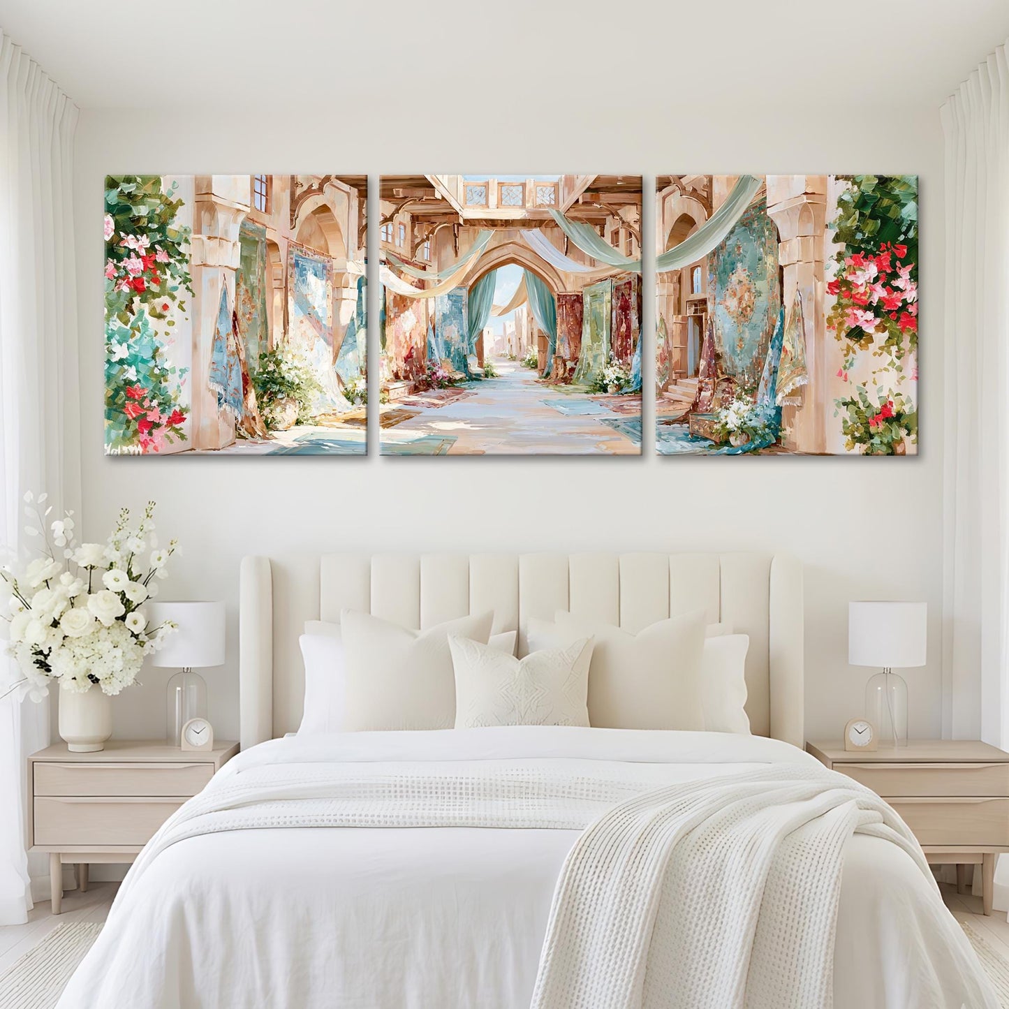 A large, three-panel painting depicting a picturesque, colorful alleyway with arches, flowers, and greenery. The painting is hung on a white wall above a bed with white bedding and pillows.