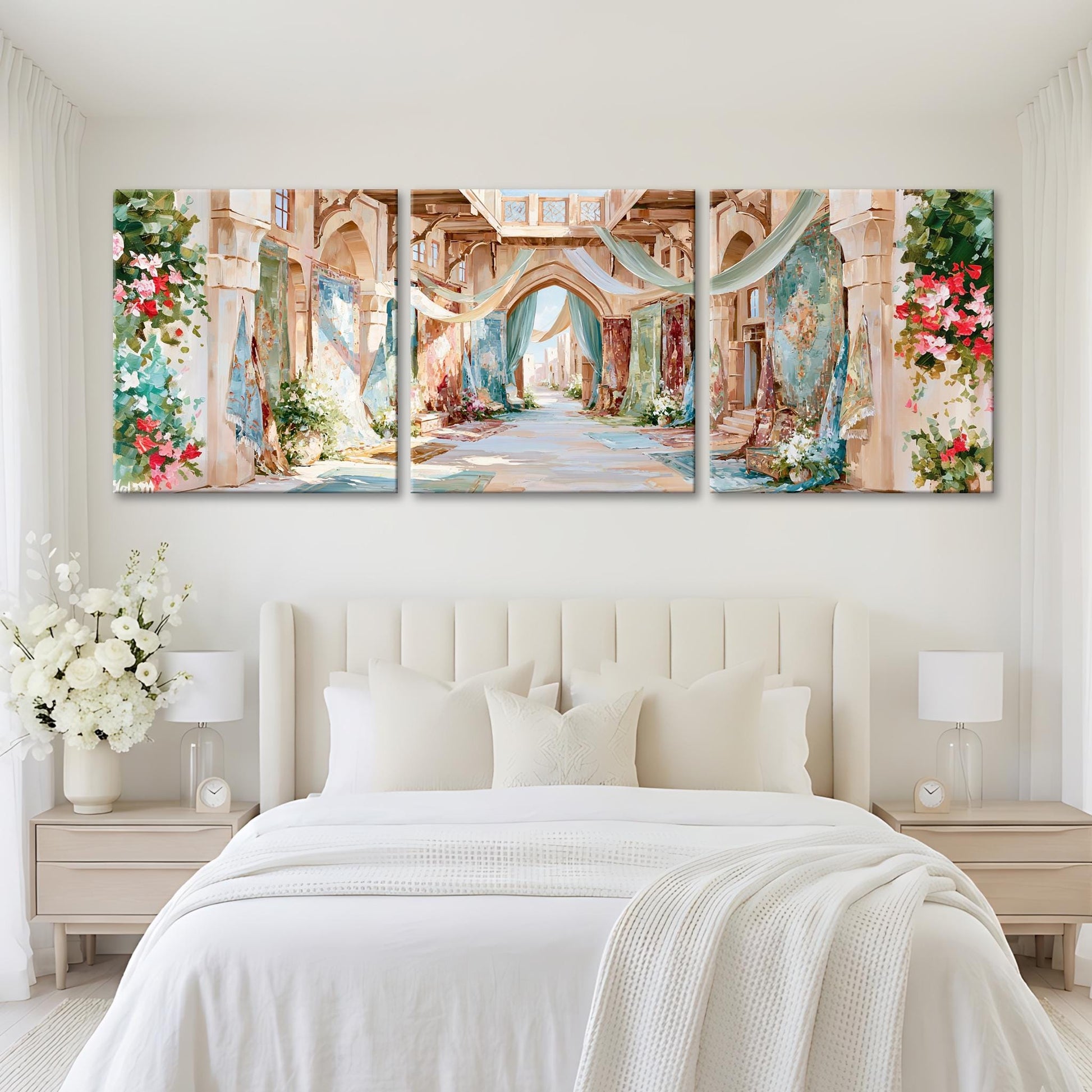 A large, three-panel painting depicting a picturesque, colorful alleyway with arches, flowers, and greenery. The painting is hung on a white wall above a bed with white bedding and pillows.