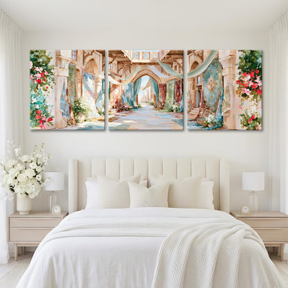 A large, three-panel painting depicting a picturesque, colorful alleyway with arches, flowers, and greenery. The painting is hung on a white wall above a bed with white bedding and pillows.