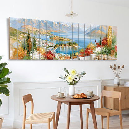 a dining area with a table set for two, featuring a vase of flowers, a plate of pastries, and two chairs. Above the table, there is a large painting depicting a scenic landscape with mountains, a lake, and colorful foliage.