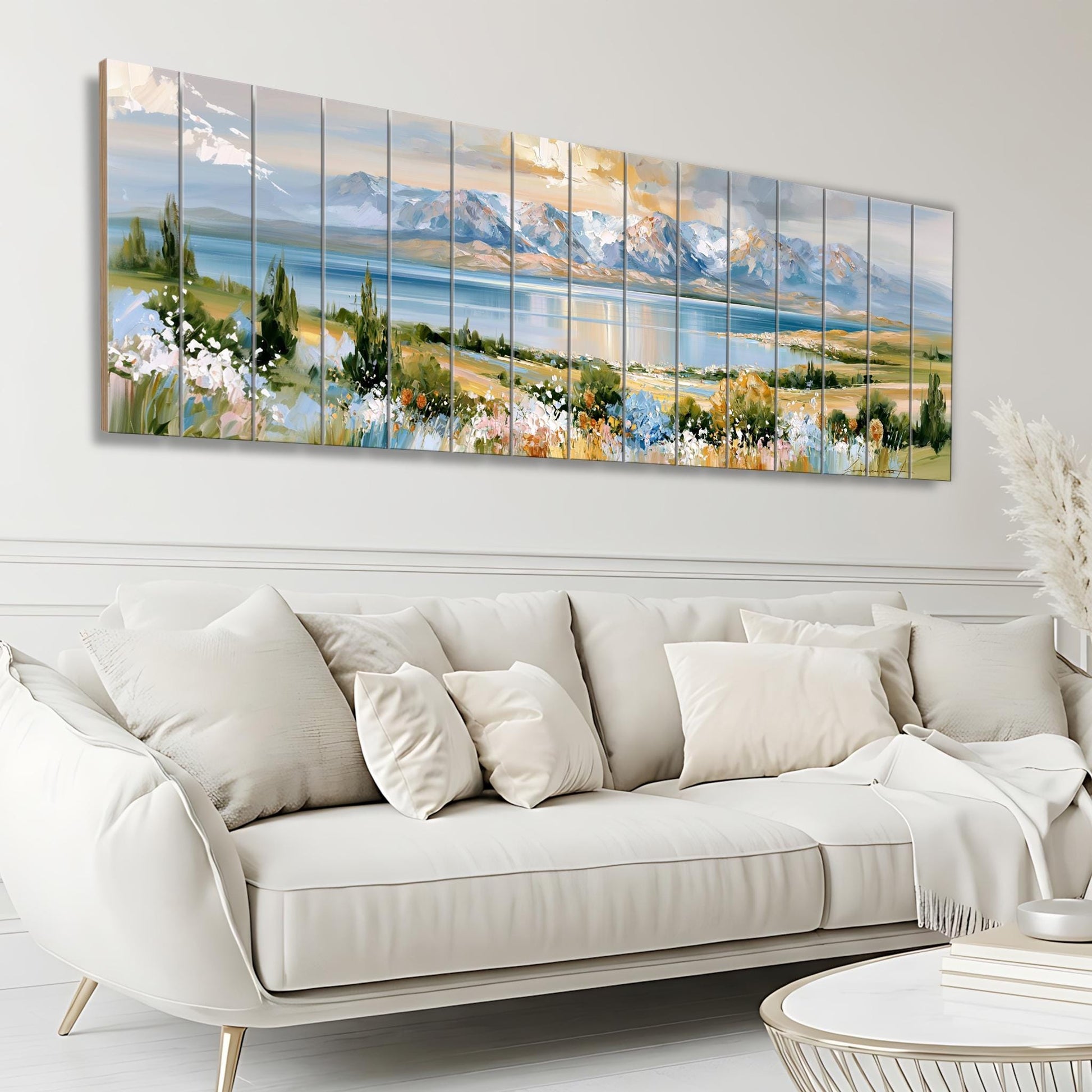 a large, white, leather couch with multiple pillows, situated in a living room setting. Above the couch, there is a large, colorful painting depicting a scenic landscape with mountains, a lake, and a blue sky with clouds.