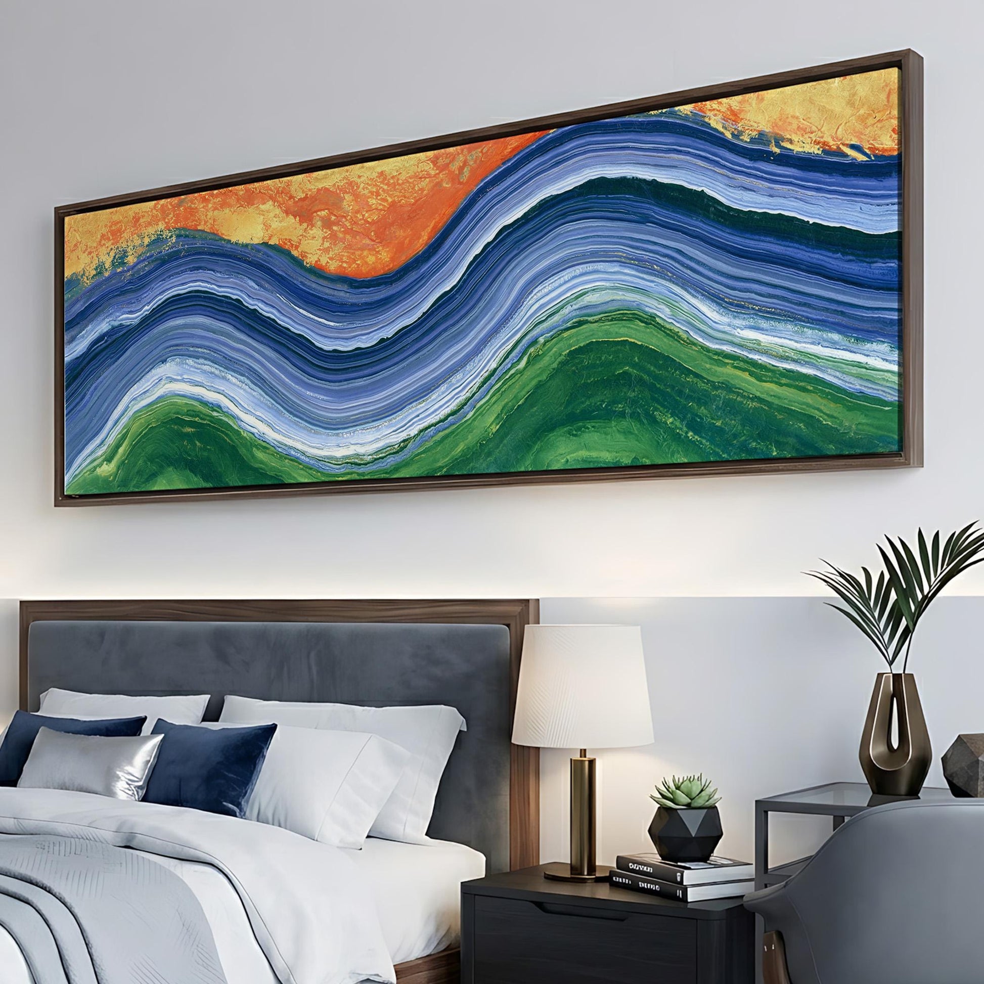 a large, colorful abstract painting hanging on a wall above a bed with white bedding and a gray headboard. The painting has a vibrant mix of blue, green, orange, and yellow colors, creating a striking visual effect. The bed is neatly made with white sheets and a gray comforter, and there is a lamp and a plant on the nightstand next to the bed.