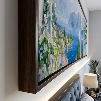 a large, framed painting of a picturesque coastal town with a river and mountains in the background.