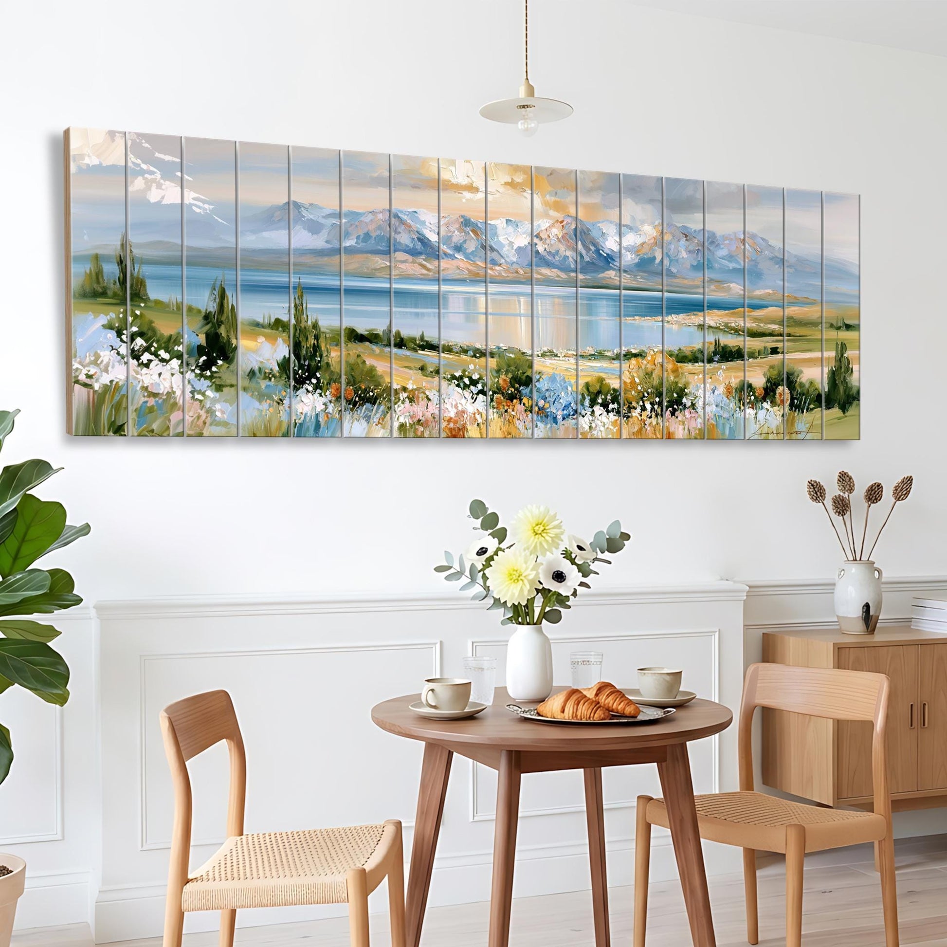 a large, colorful painting of a landscape with mountains, flowers, and a lake, hanging on a wall above a wooden dining table with two chairs.