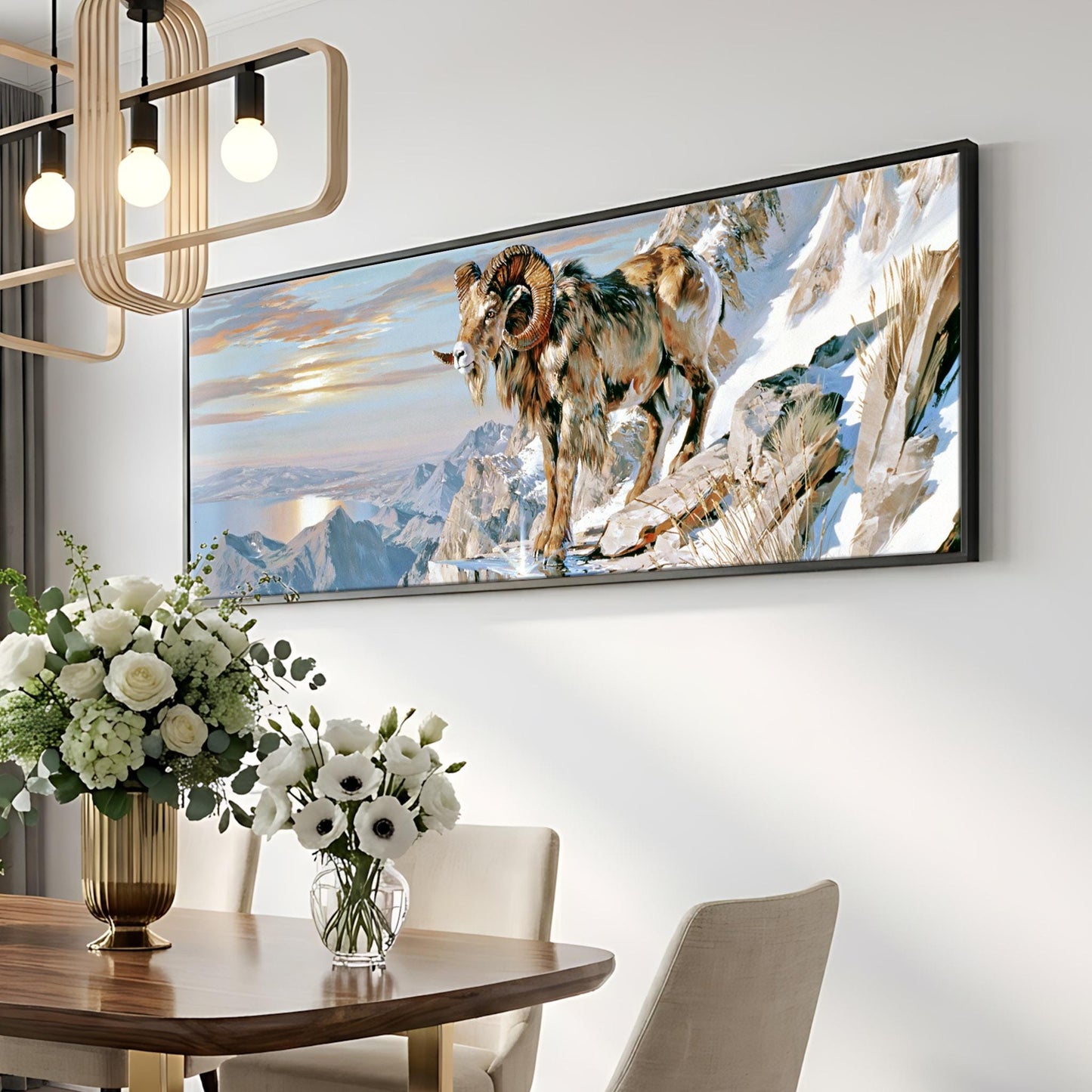 a large framed painting of a ram standing on a snowy mountain, hanging on a wall above a dining table with a vase of white flowers.