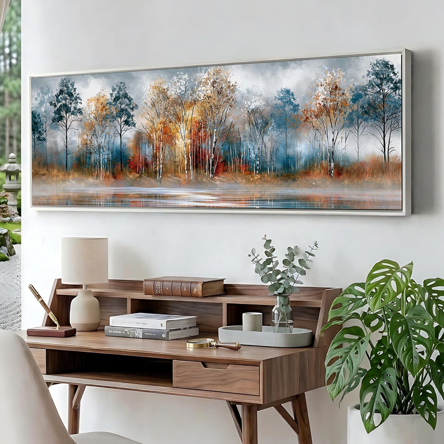 a large painting of a forest scene hanging on a wall above a wooden desk with a lamp, books, and a plant.
