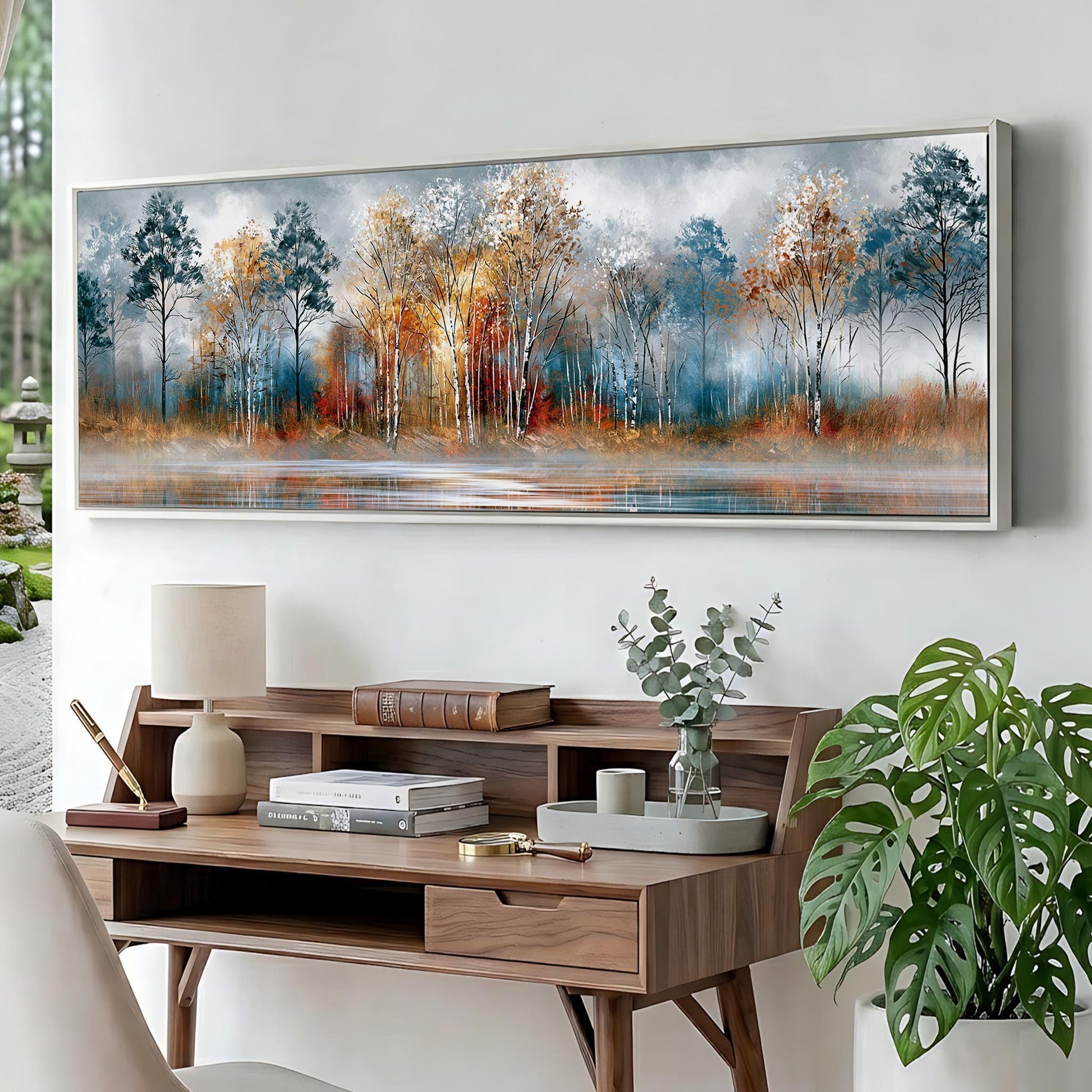 a large painting of a forest scene hanging on a wall above a wooden desk with a lamp, books, and a plant.