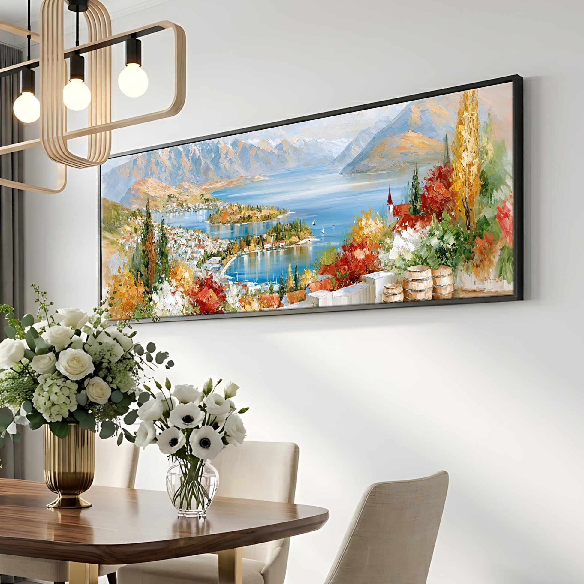 a large painting of a scenic landscape hanging on a wall above a dining table with a vase of flowers.