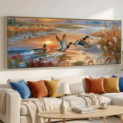a large painting of ducks swimming in a lake, with a warm sunset in the background. The painting is hung on a wall above a white couch with colorful throw pillows.