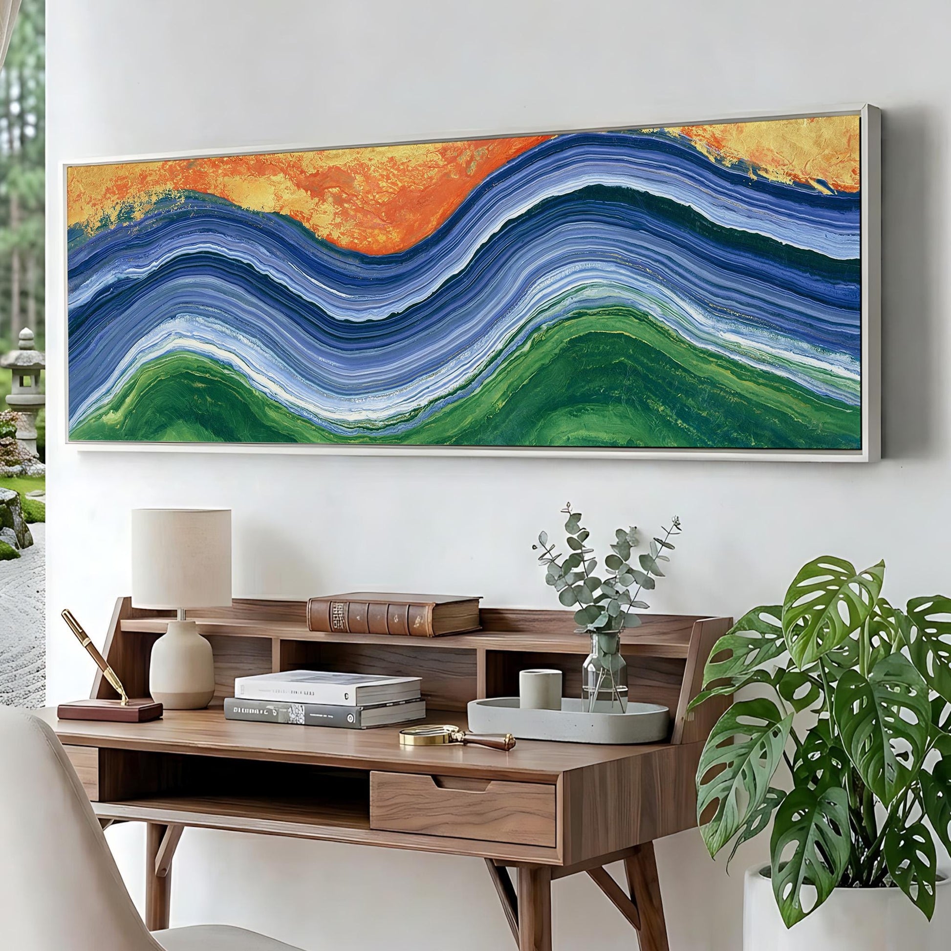 a large, colorful abstract painting hanging on a wall above a wooden desk with various items on it, including a lamp, books, and a vase with greenery.