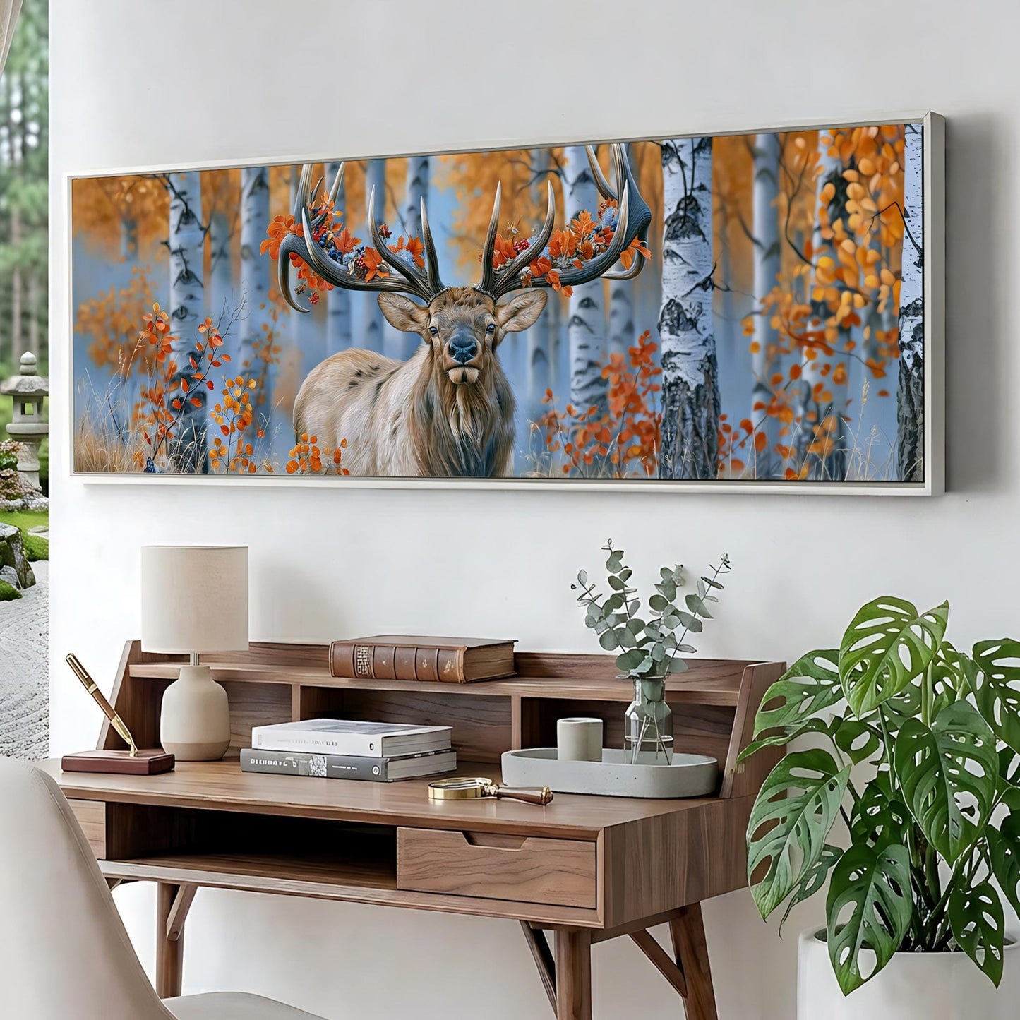 a large framed painting of a deer with antlers in a forest setting, hanging on a wall above a wooden desk with various items on it.