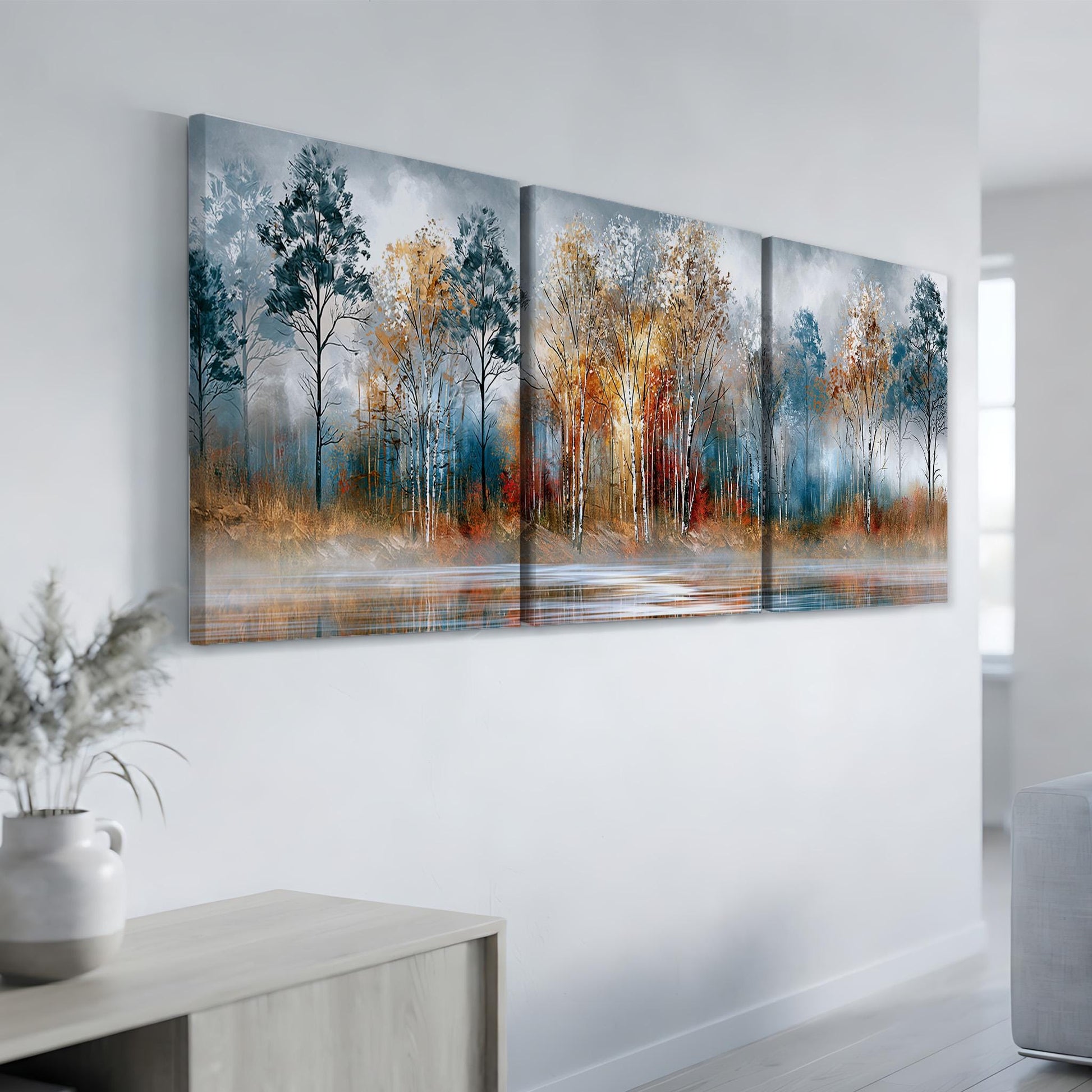 a large, three-panel landscape painting hanging on a white wall. The painting depicts a serene forest scene with trees in various shades of blue, orange, and yellow, set against a calm body of water.