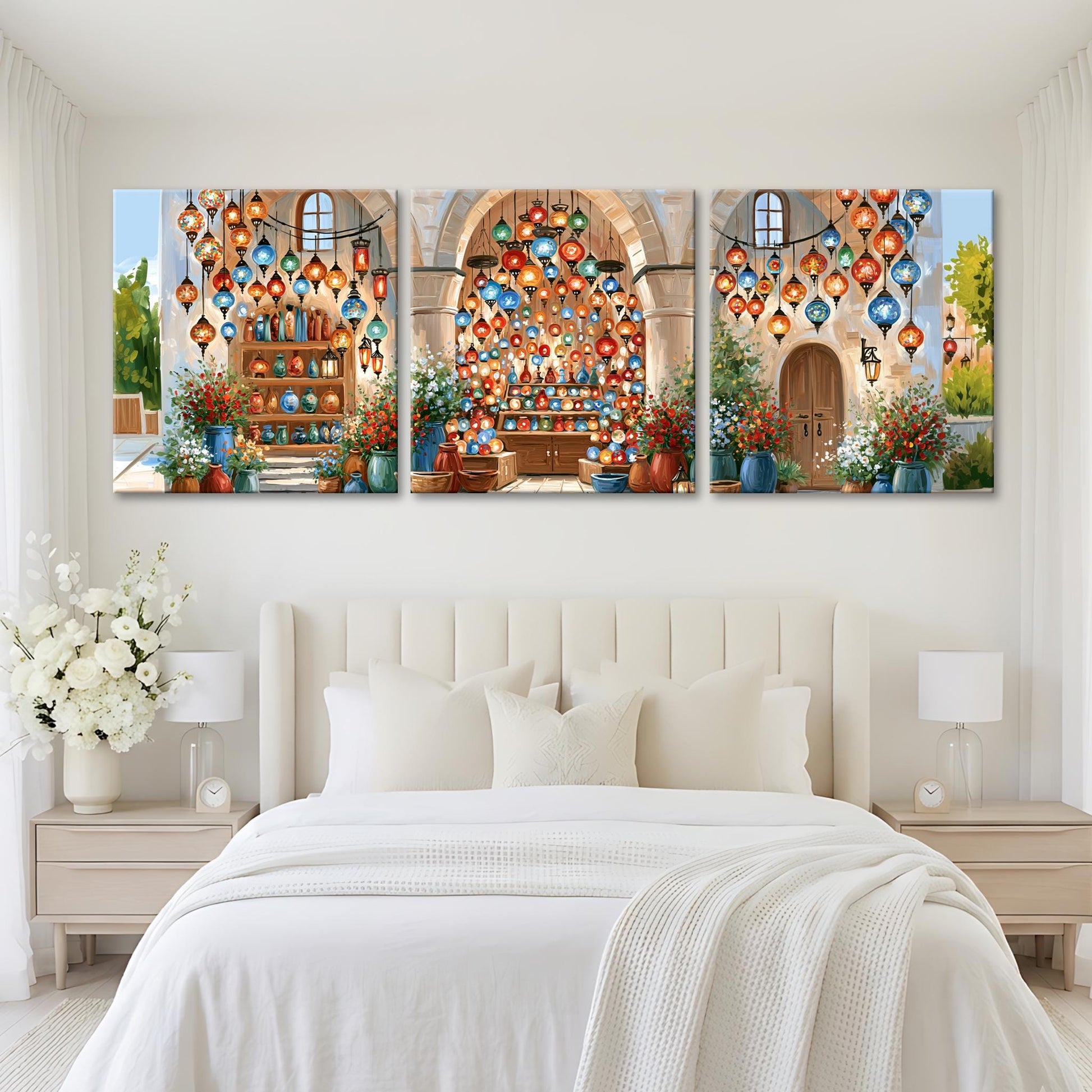 A bedroom with a large bed and white bedding, flanked by nightstands with lamps. Above the bed are three large paintings depicting colorful lanterns and flowers, creating a festive and decorative atmosphere.