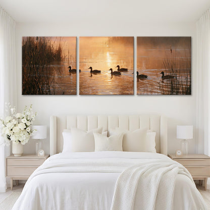 A bedroom with a large bed and white bedding, along with two nightstands on either side. Above the bed, there is a large, three-panel artwork depicting ducks swimming in a body of water, with the sun rising in the background.