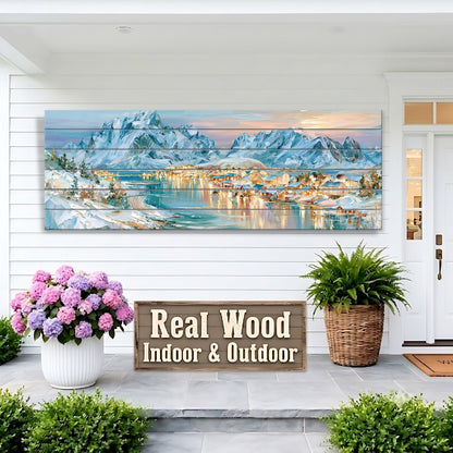a large wooden panel hanging on a white wall, depicting a scenic mountain landscape with a town in the distance. The panel is mounted above a wooden sign that reads "Real Wood Indoor & Outdoor". The sign is placed on a porch, with two potted plants and a large bouquet of pink flowers nearby.