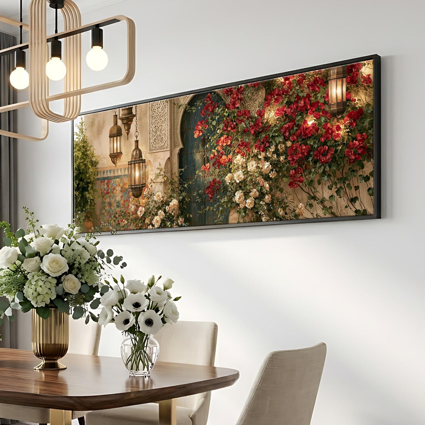 a dining room with a large floral painting hanging on the wall above a wooden table. The table is set with a vase of white flowers and a potted plant. The room has a modern and elegant design, with a chandelier and a white wall.