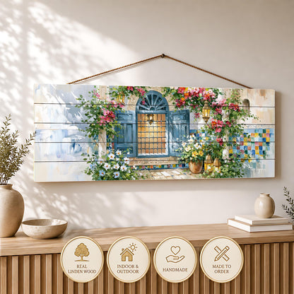 a wooden wall hanging with a painting of a colorful, flower-filled window. The painting is hanging on a wall, and there are several decorative items placed below it, including a vase, a bowl, and a stack of books.