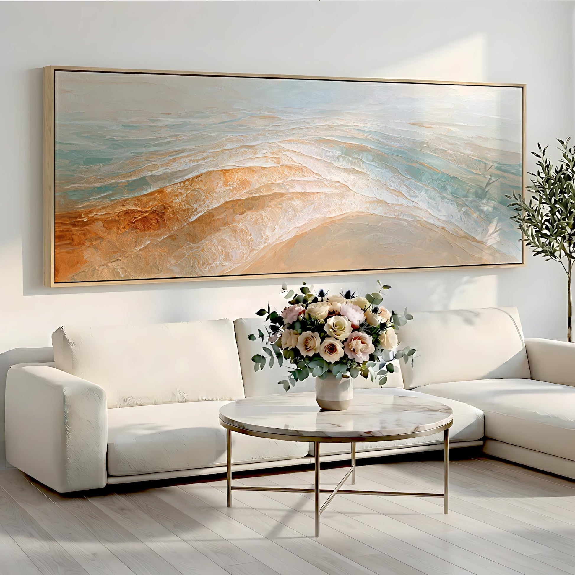 a living room with a large painting of a beach scene hanging on the wall above a white sofa. In front of the sofa, there is a round coffee table with a vase of flowers on it.
