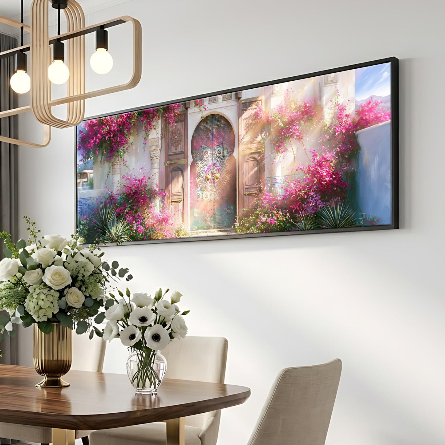 a large, framed painting of a colorful, floral-adorned building hanging on a wall above a dining table with a vase of white flowers.