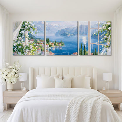 A large, three-panel painting depicting a scenic view of a coastal town with mountains in the background, framed by a window.