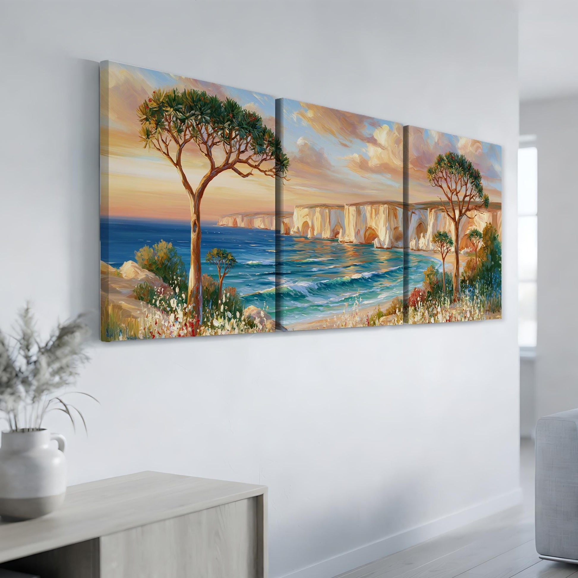 a large, three-panel landscape painting hanging on a white wall. The painting depicts a serene coastal scene with a tree, a bridge, and the ocean in the background.